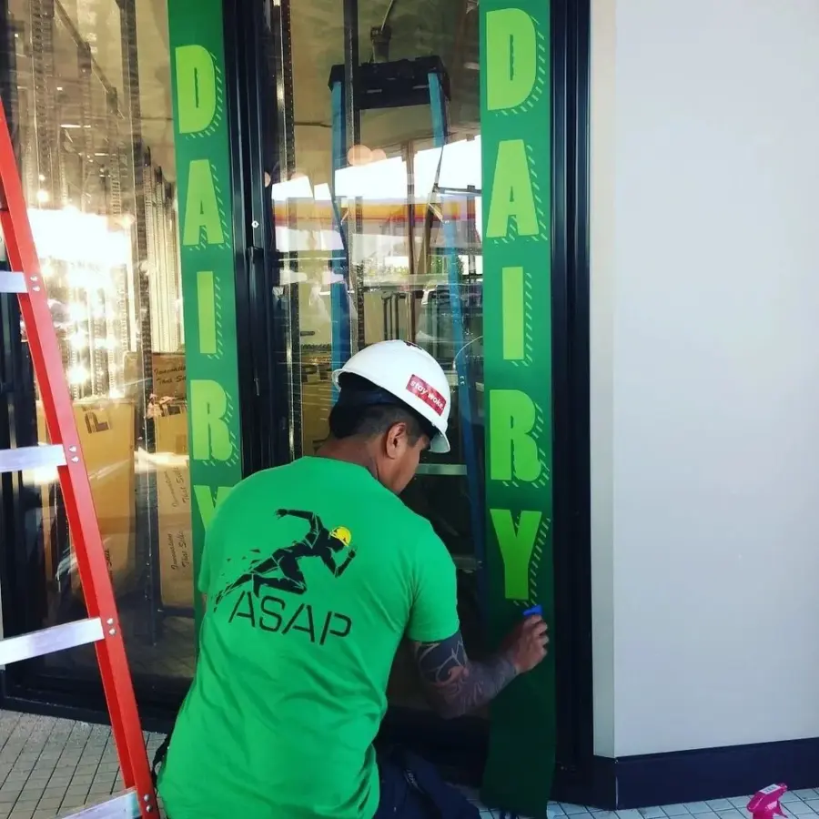 Technician installing custom window graphics and vinyl lettering on commercial storefront glass